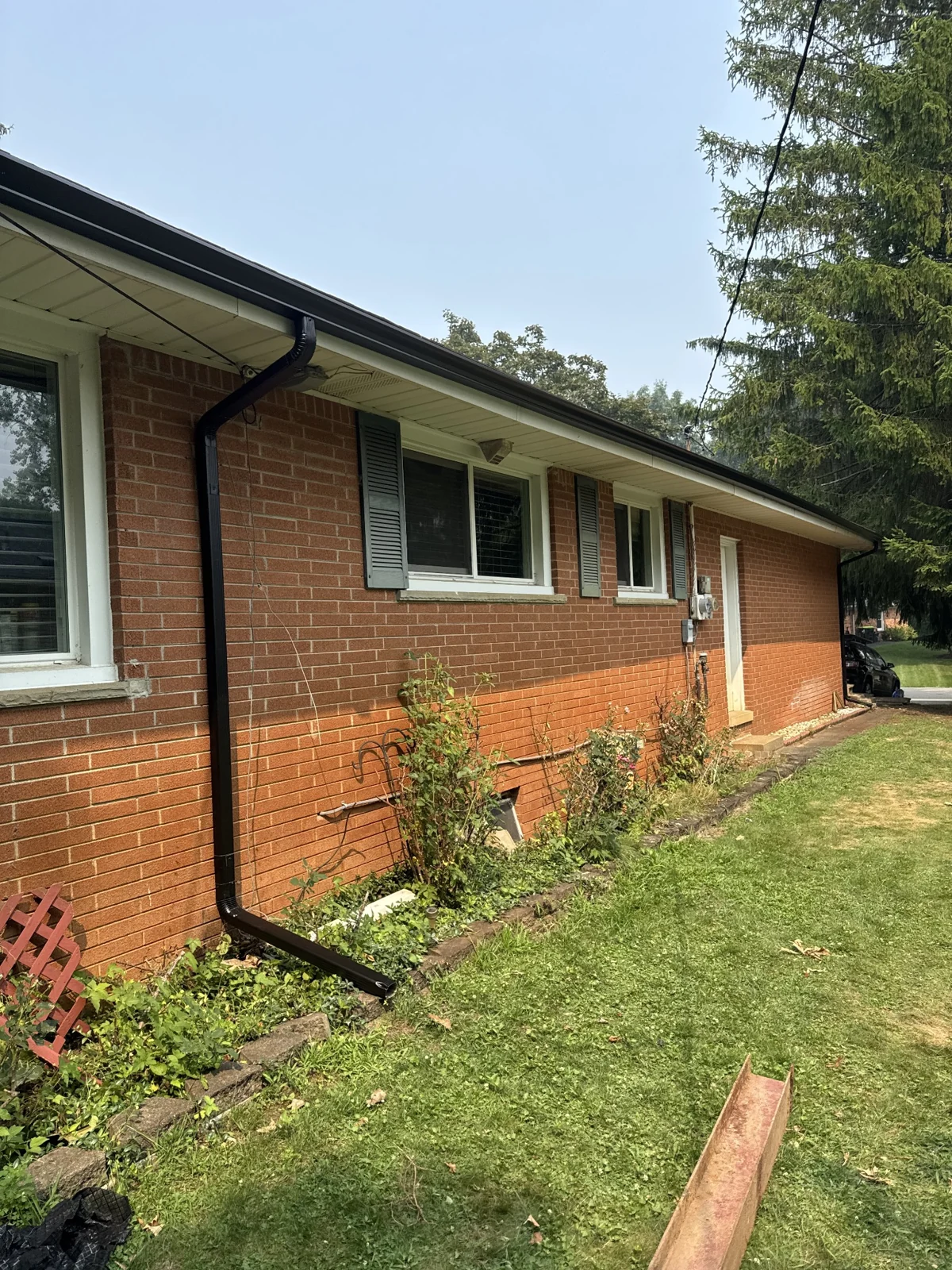 Dark seamless gutters and downspout installed on a brick home