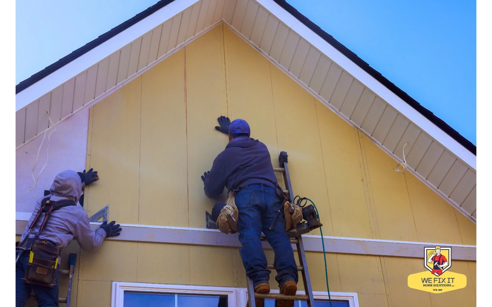 Workers fitting siding panels beneath a roof gable